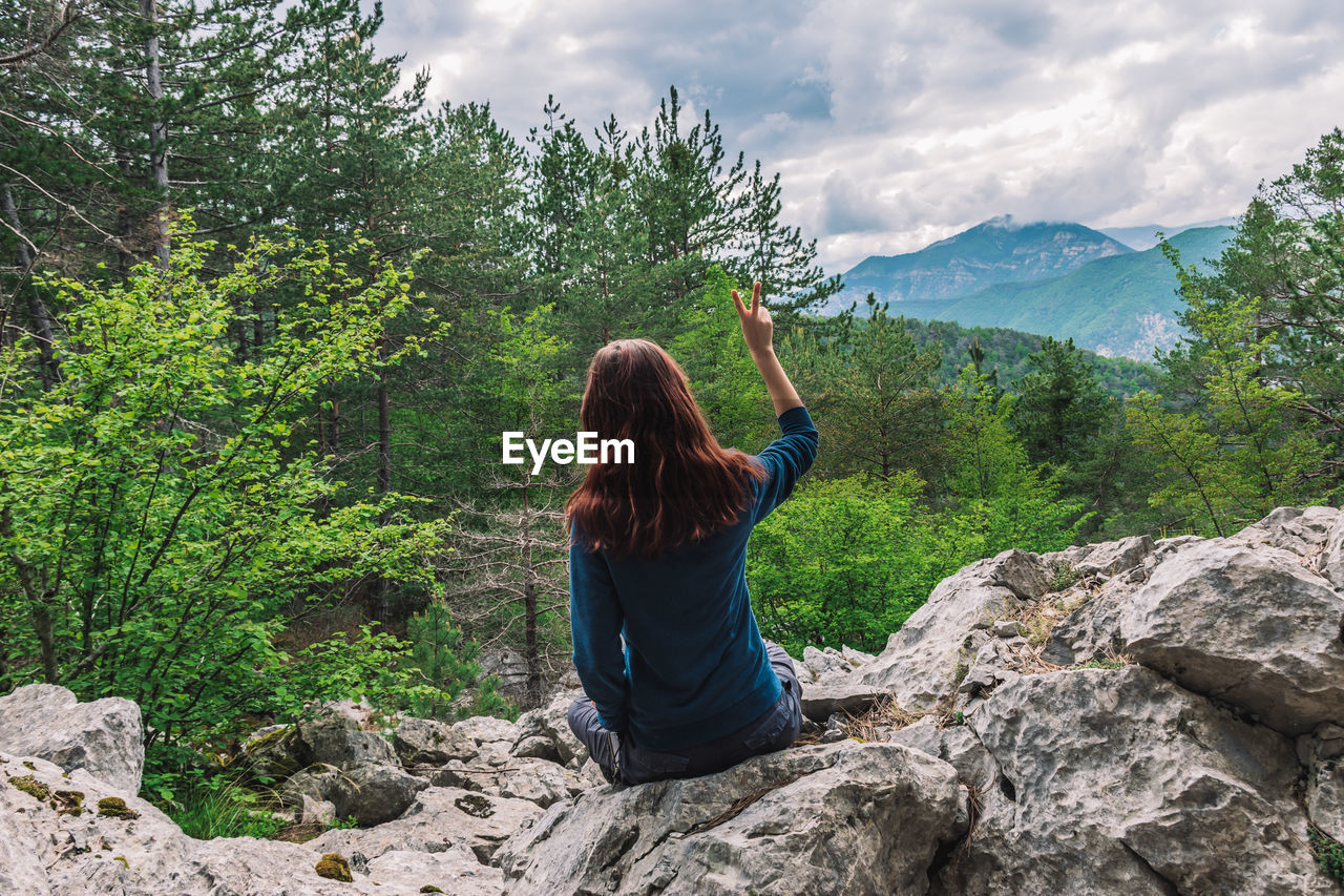 REAR VIEW OF WOMAN WALKING ON ROCKS AGAINST SKY
