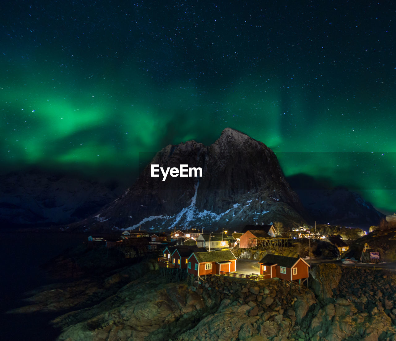 Illuminated houses by mountain against aurora borealis in sky at night