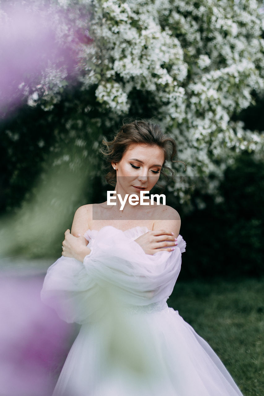 Beautiful bride in a wedding dress walks in a blooming apple-tree park in spring