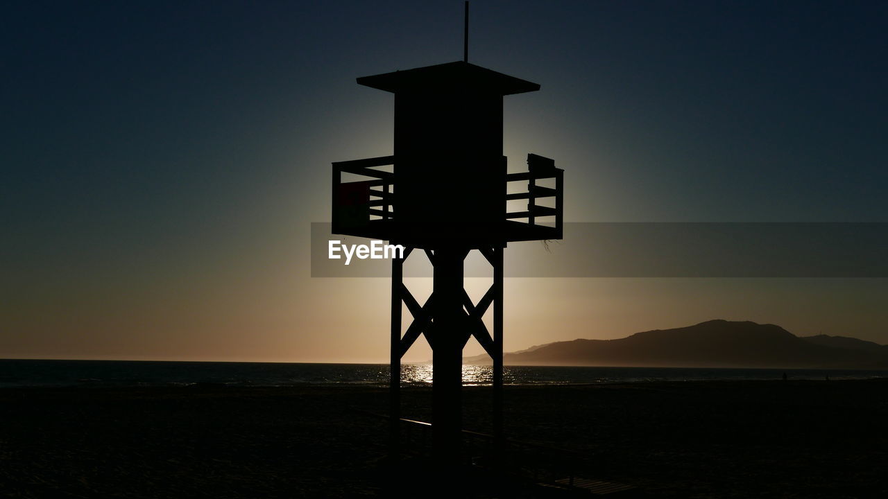 Silhouette cross on beach against sky during sunset