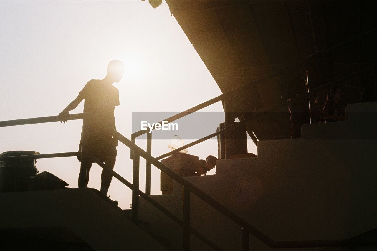 LOW ANGLE VIEW OF SILHOUETTE MAN STANDING ON STAIRCASE AGAINST SKY