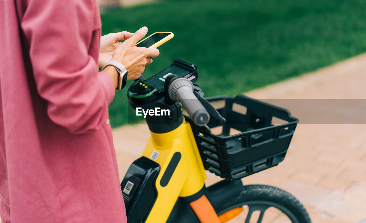 Unrecognizable cropped woman rents an electric city bike using an app on her phone.