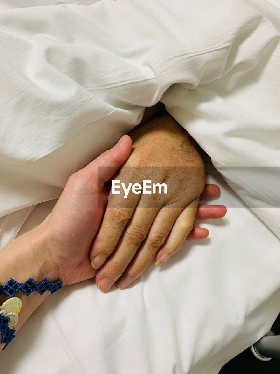 Cropped image of people holding hands on bed at hospital