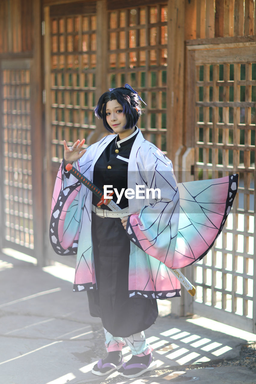 portrait of young woman with umbrella standing against building