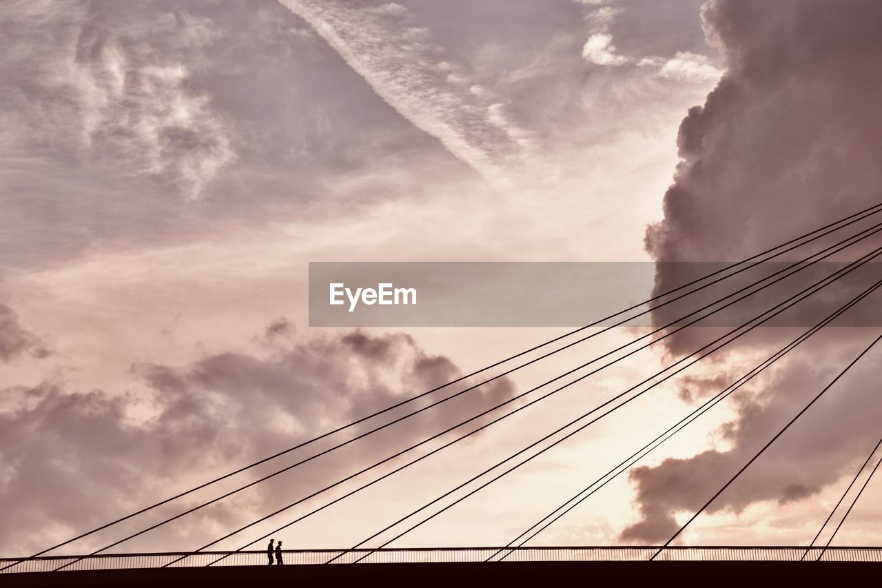 Low angle view of silhouette bridge against cloudy sky during sunset