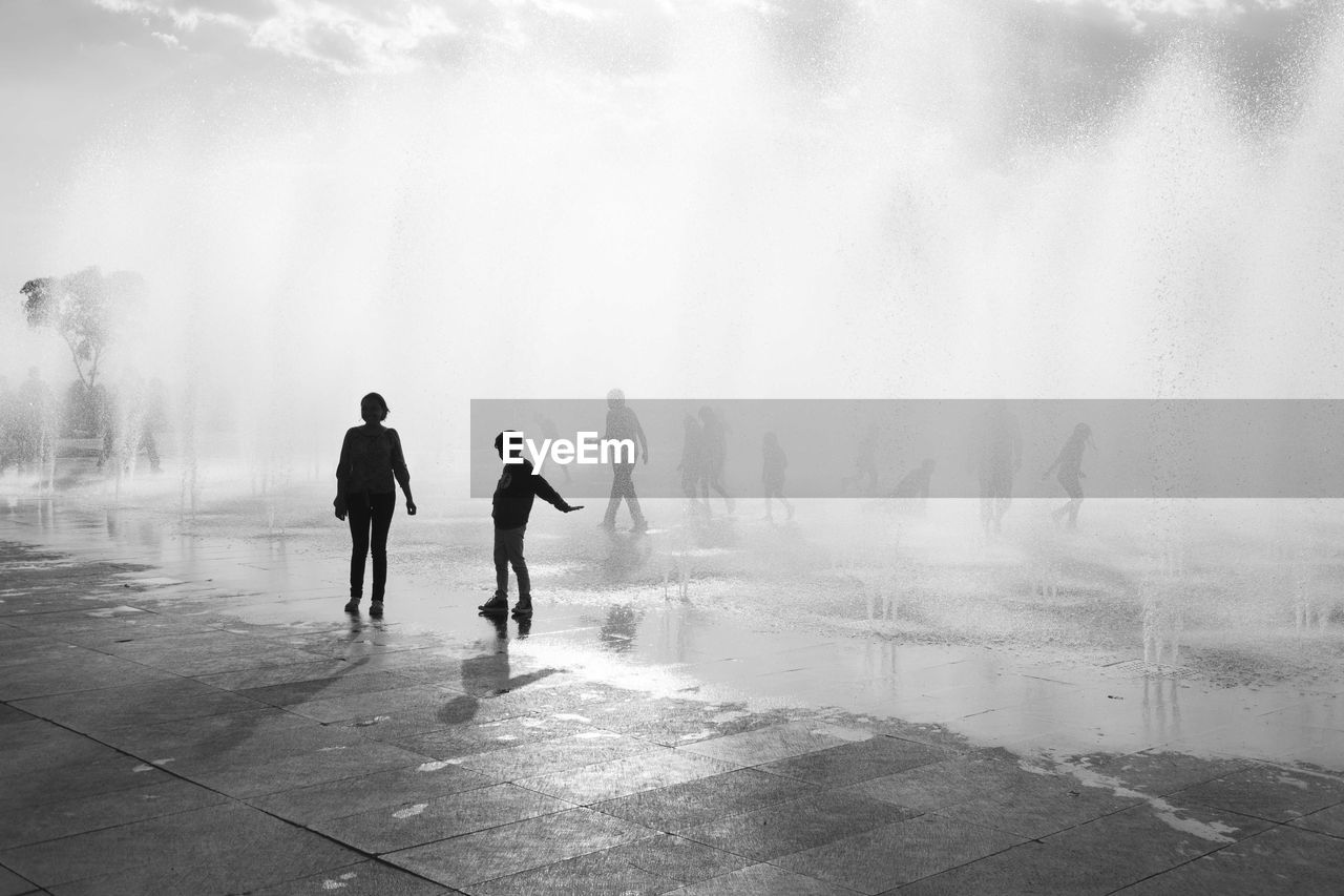 SILHOUETTE OF PEOPLE WALKING ON WET SHORE DURING WINTER