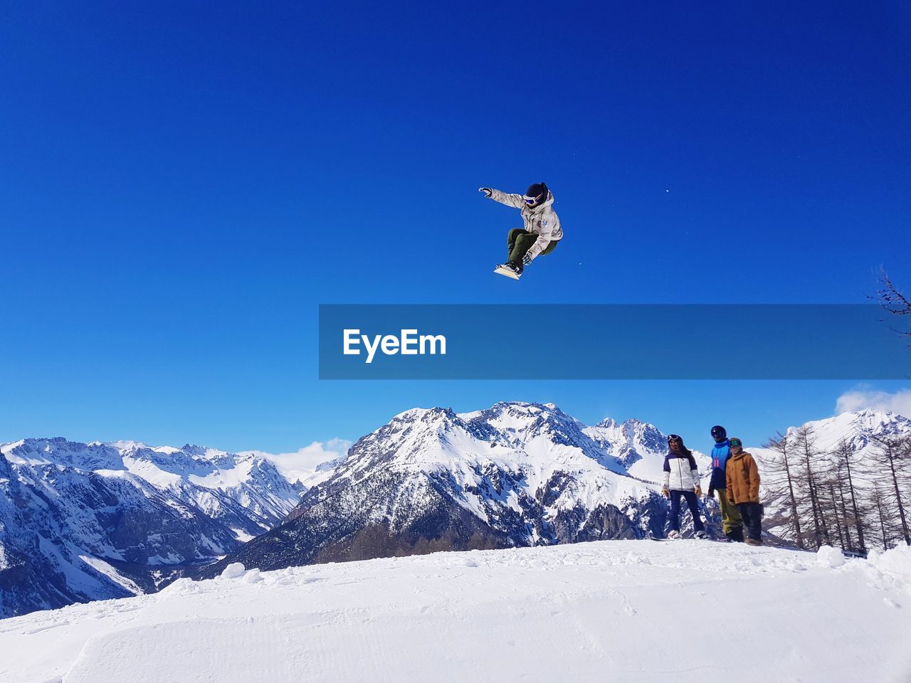 People jumping on snowcapped mountain against clear sky