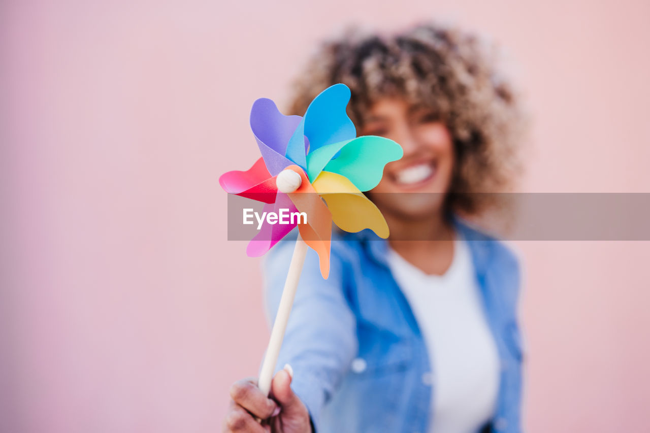 Beautiful happy hispanic woman with afro hair holding colorful pinwheel. pink background,wind energy