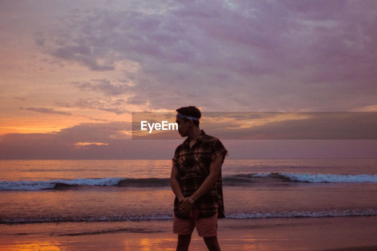 Man standing on shore at beach during sunset