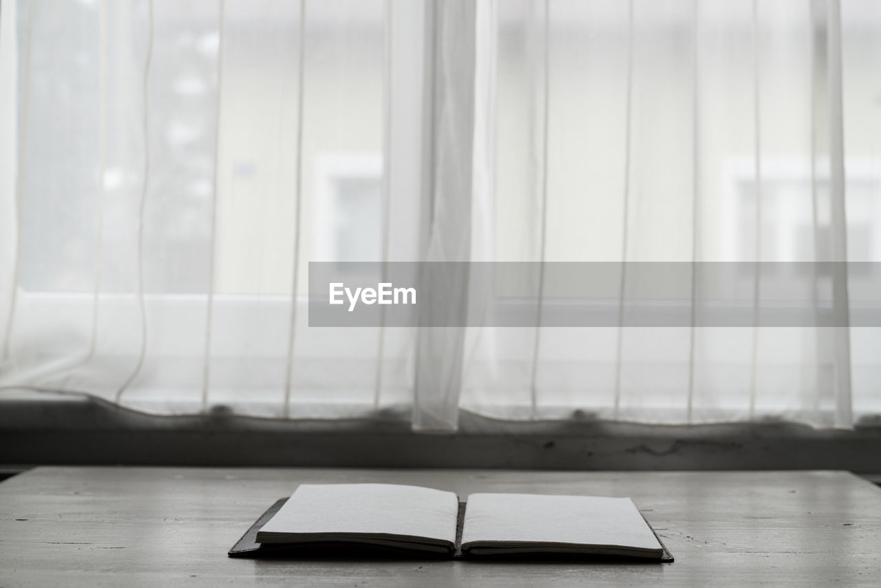 CLOSE-UP OF OPEN BOOK ON TABLE AGAINST WINDOW