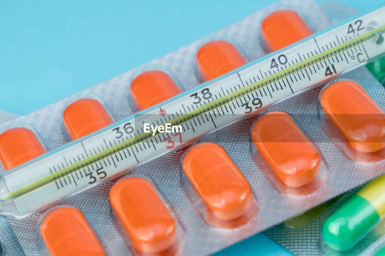 Blisters with pills and thermometer lie on a blue background closeup