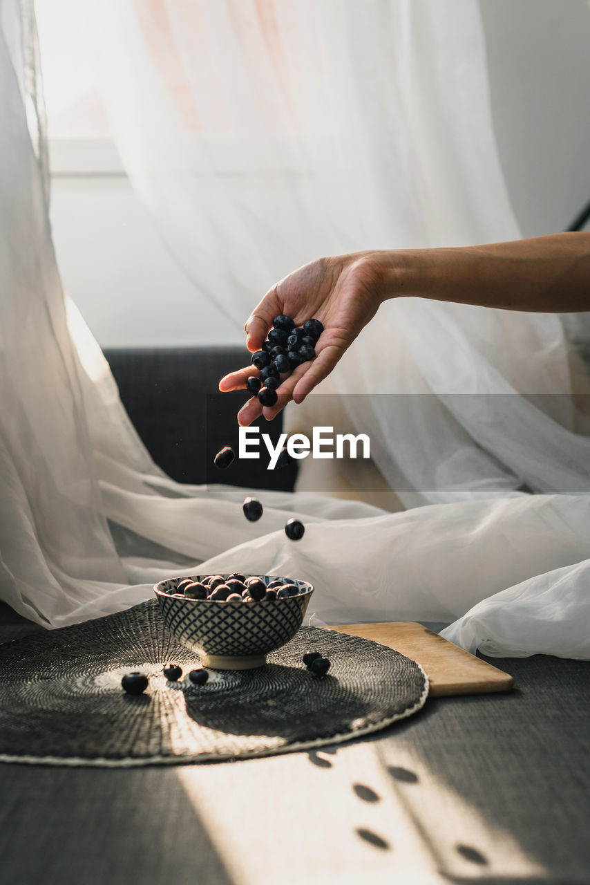 A woman's hand tossing blueberries into a small plate. it's under a kitchen board.