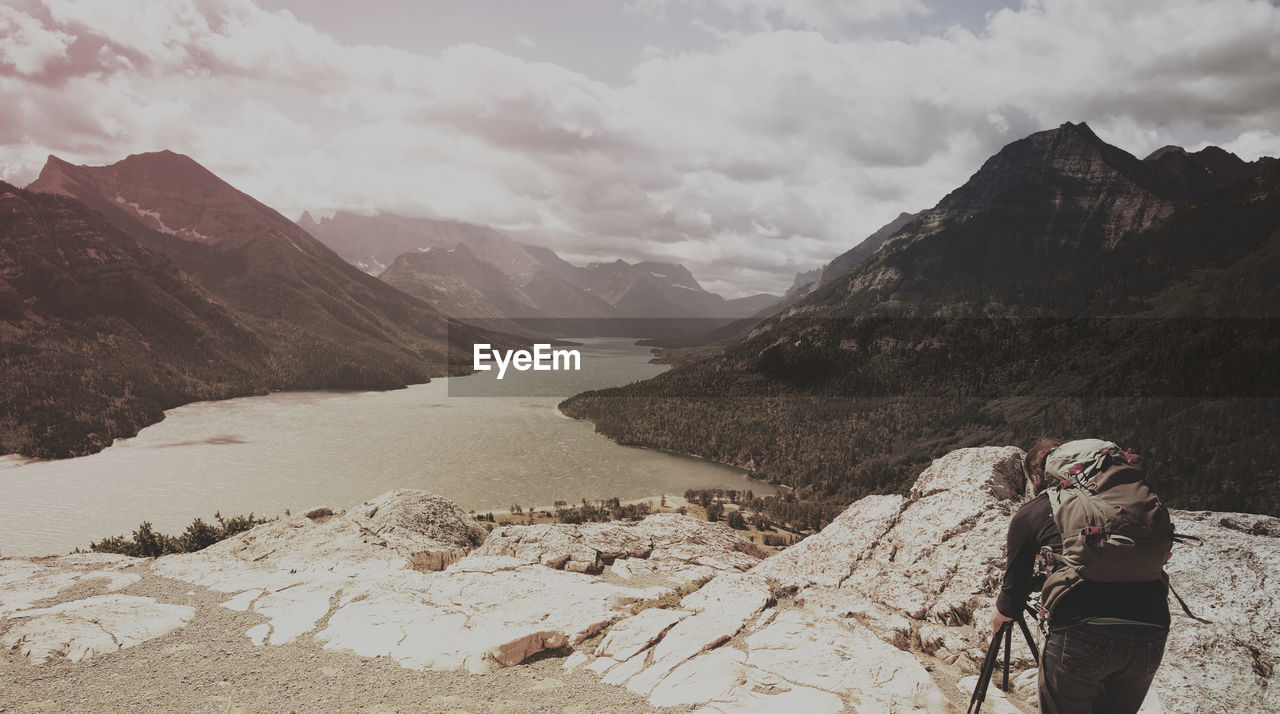 Rear view of woman photographing mountains against cloudy sky