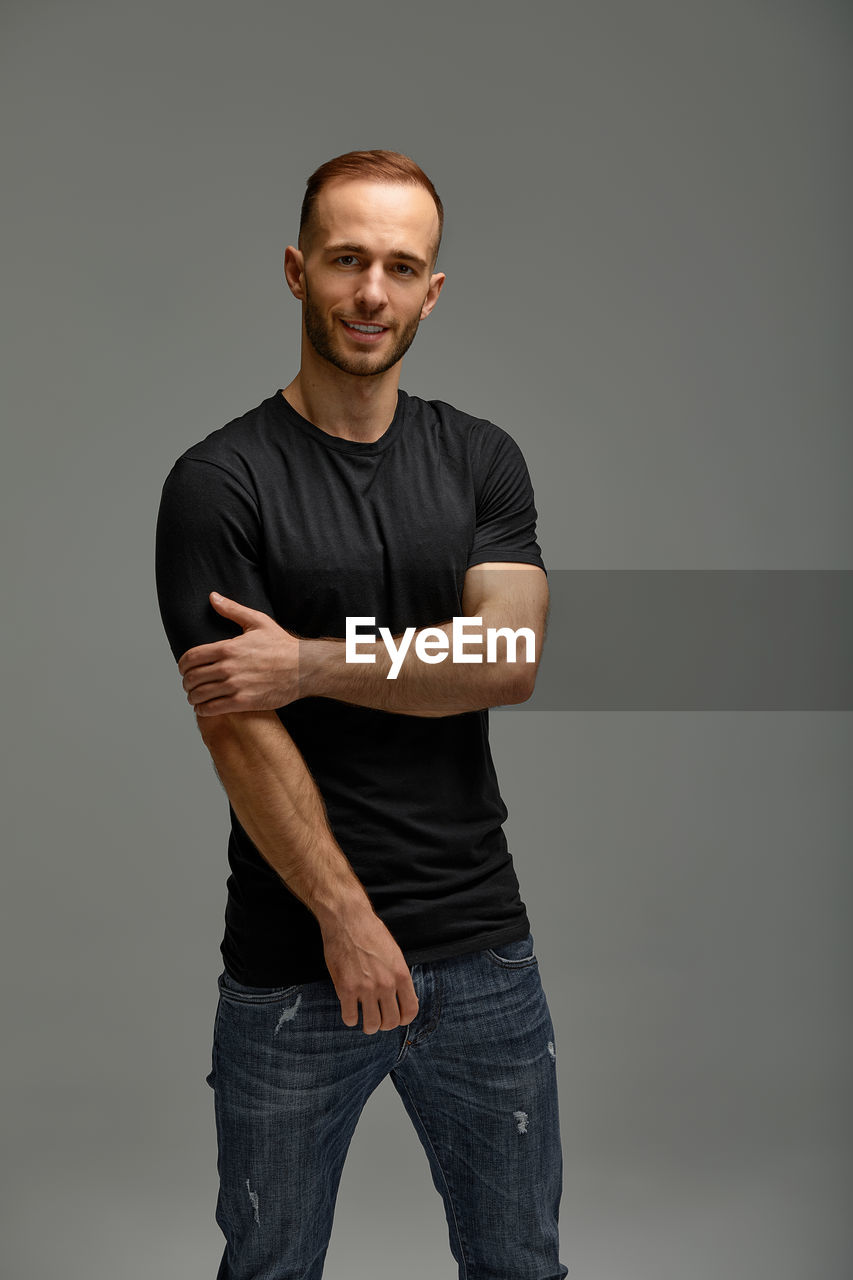 portrait of young man with arms crossed standing against black background