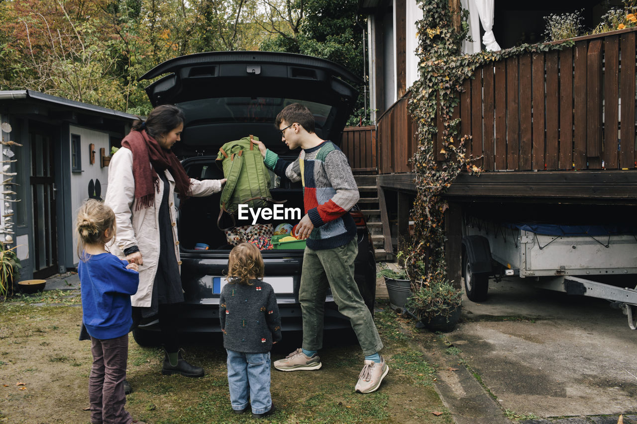 Family preparing for picnic while loading stuff in electric car trunk
