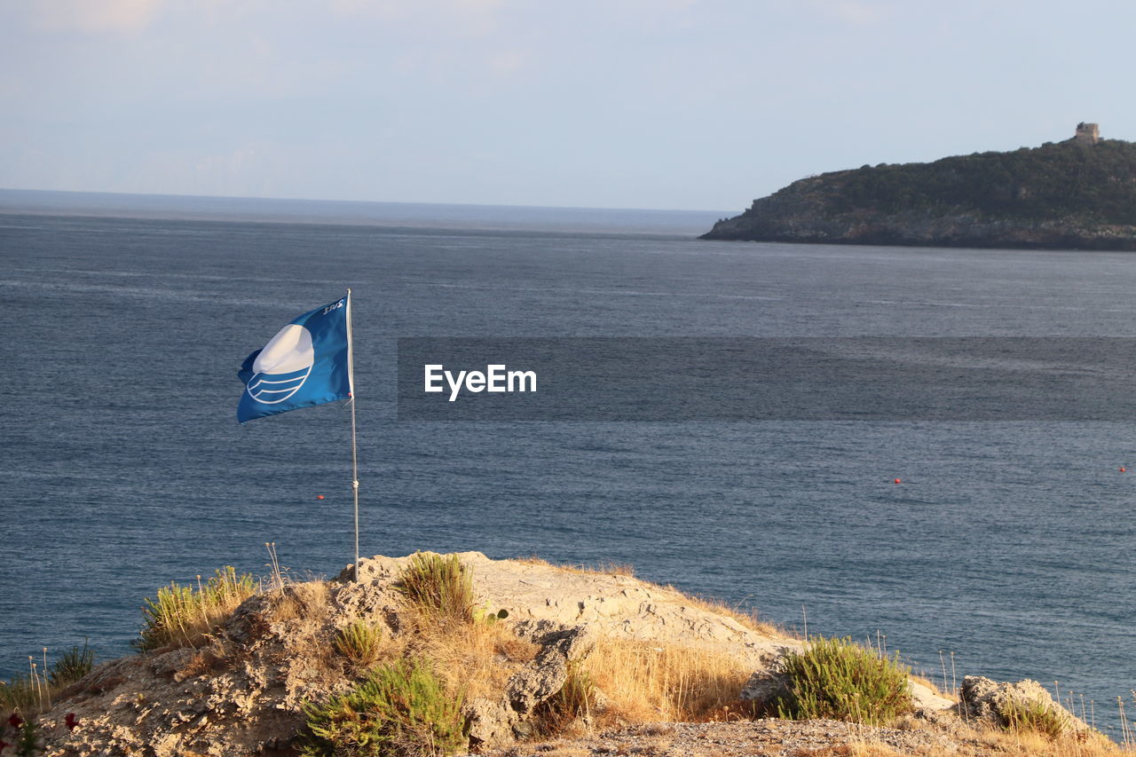 water, sea, coast, ocean, shore, sky, flag, nature, scenics - nature, land, bay, beauty in nature, beach, patriotism, body of water, tranquility, tranquil scene, day, no people, horizon, cliff, horizon over water, terrain, rock, non-urban scene, vacation, tower, outdoors, environment, cove, blue, idyllic, travel, travel destinations, coastline, cloud, mountain, guidance, transportation, wave