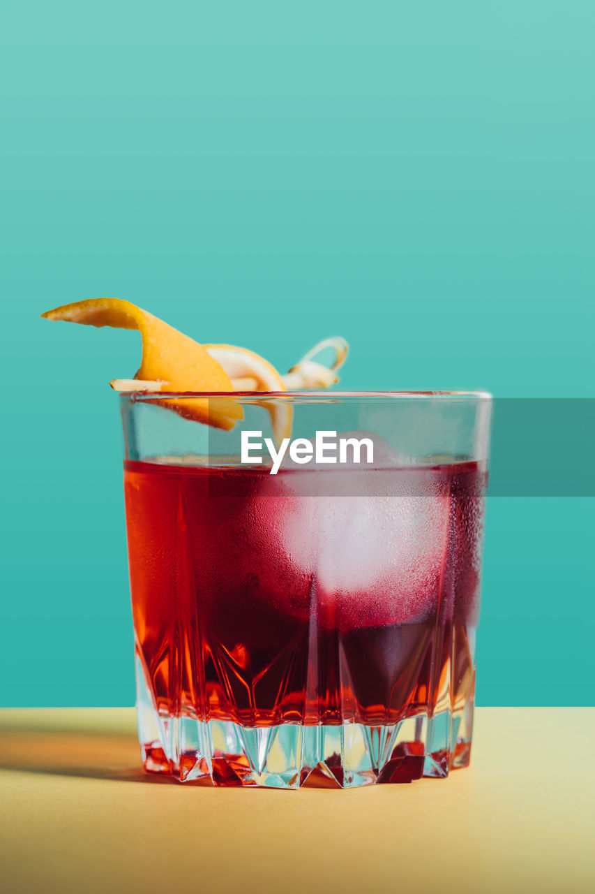 Glass of bitter alcoholic negroni cocktail served with ice and orange peel on light surface