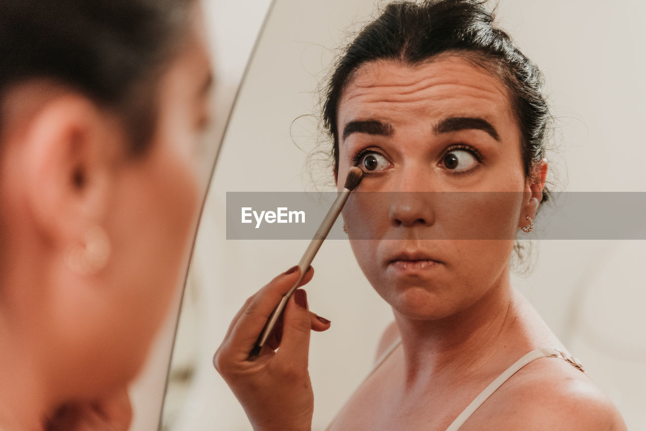 Mirror photo of beautiful young woman putting on makeup