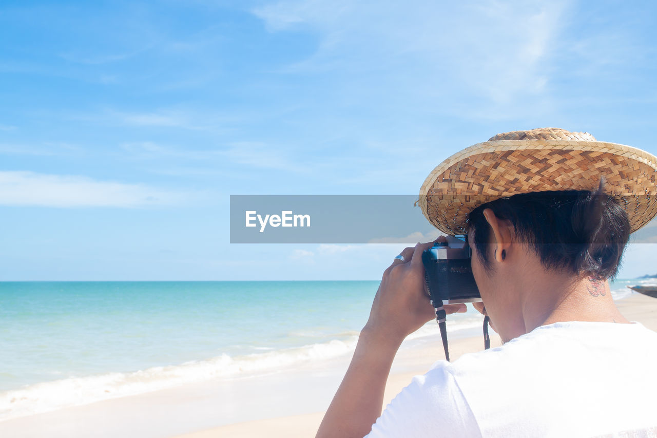 Rear view of man photographing sea during sunny day