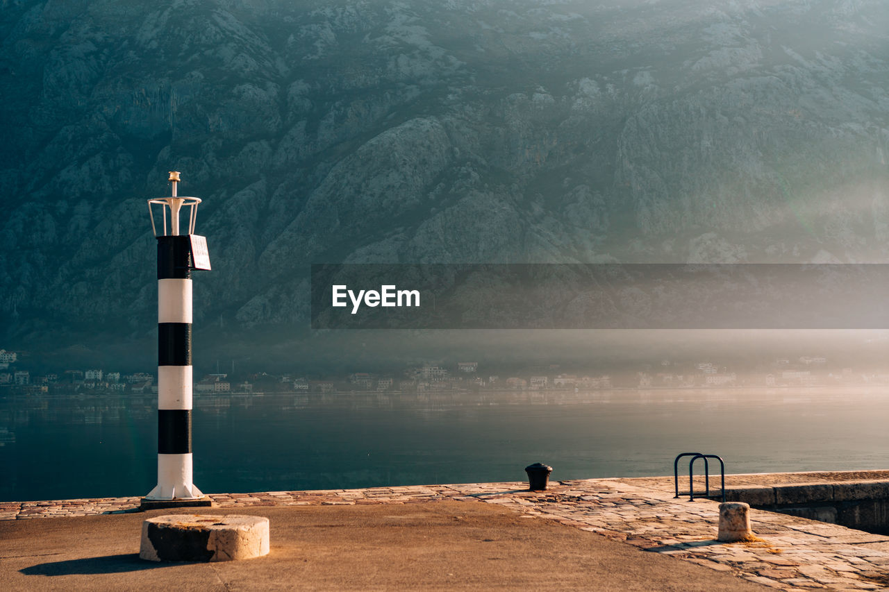 LIGHTHOUSE AMIDST SEA AGAINST MOUNTAIN