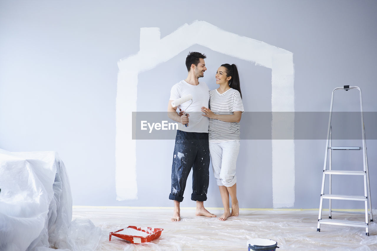 Happy couple painting in new apartment with house shape on wall