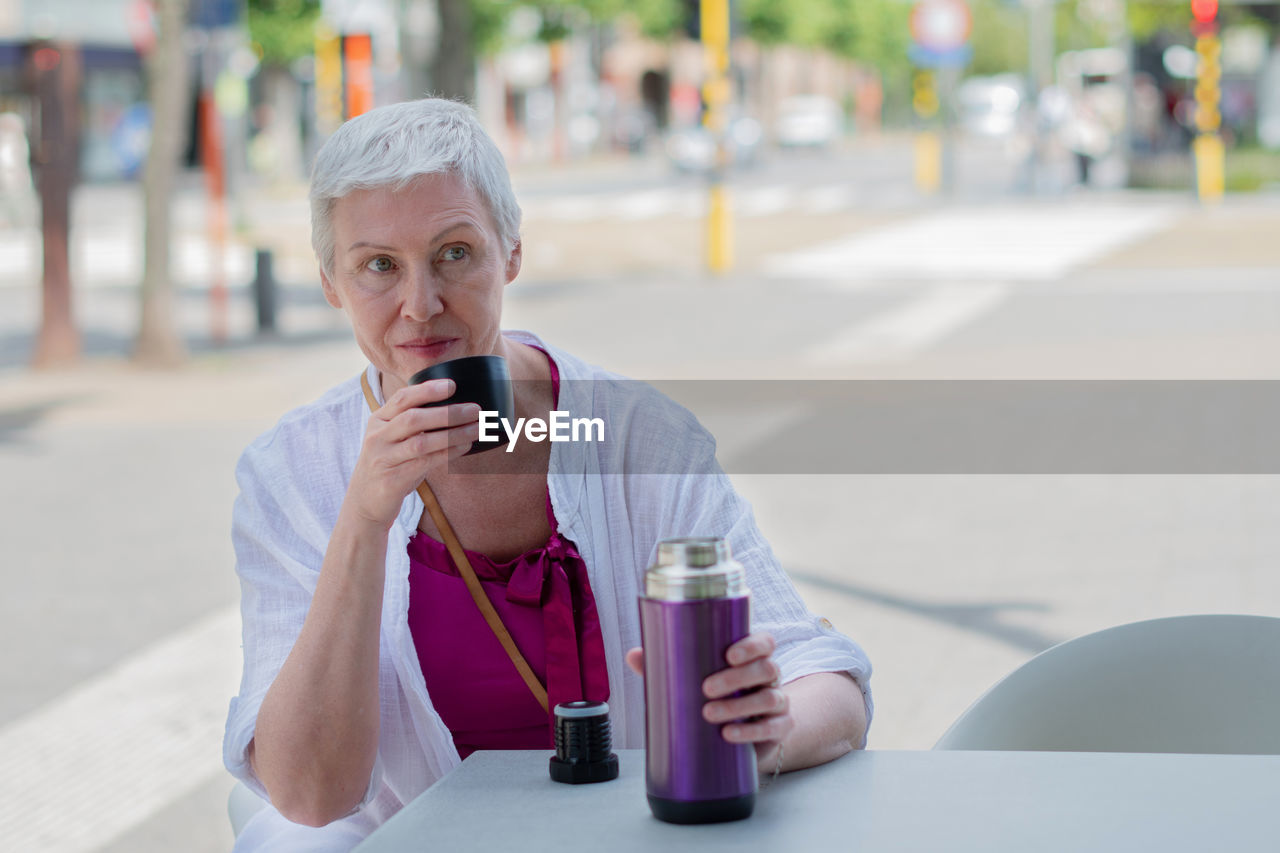 An aged woman with bob cut drink water from plastic bottle at the cafe table