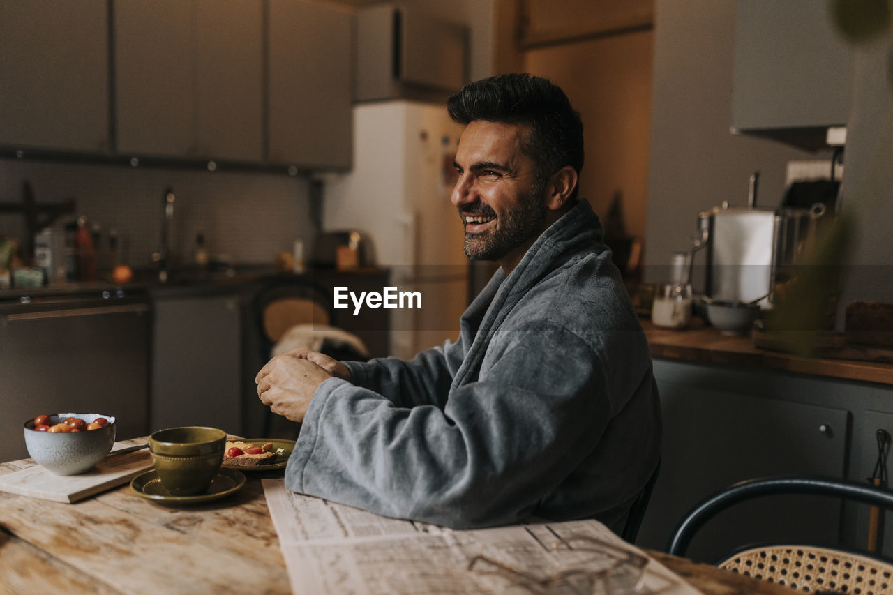 Happy man wearing bathrobe while having breakfast at home