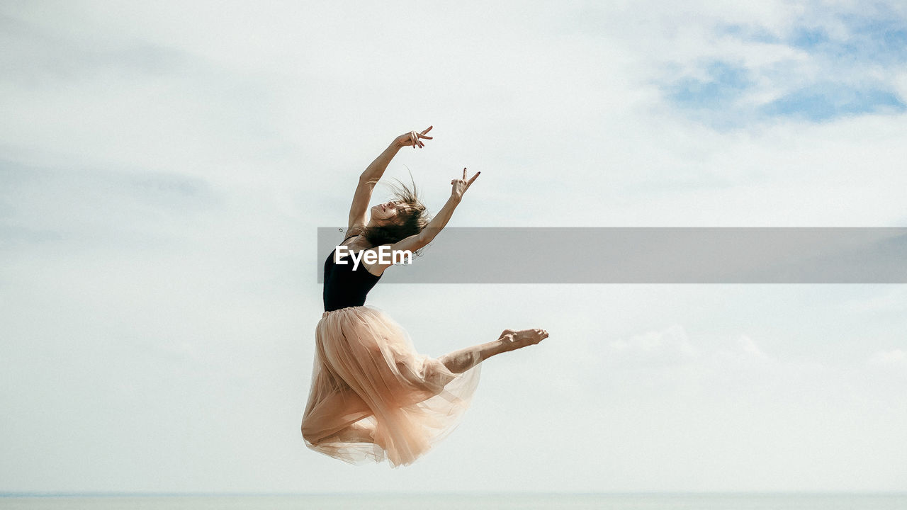 Woman dancing over sea against sky