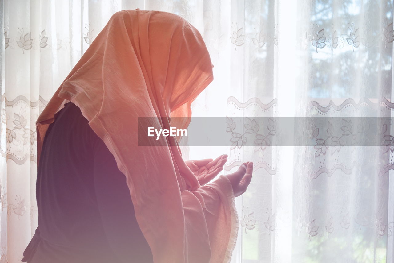 SIDE VIEW OF WOMAN STANDING AGAINST CURTAIN