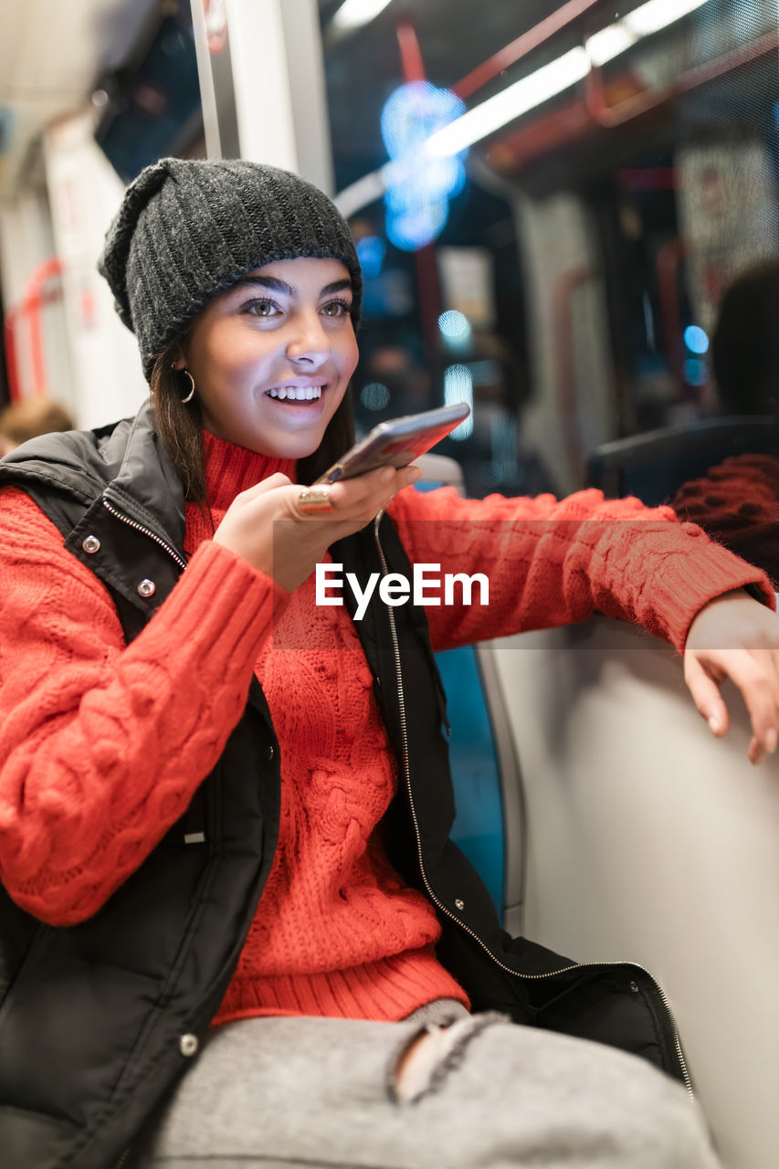 Cheerful young woman talking through mobile phone speaker in tram