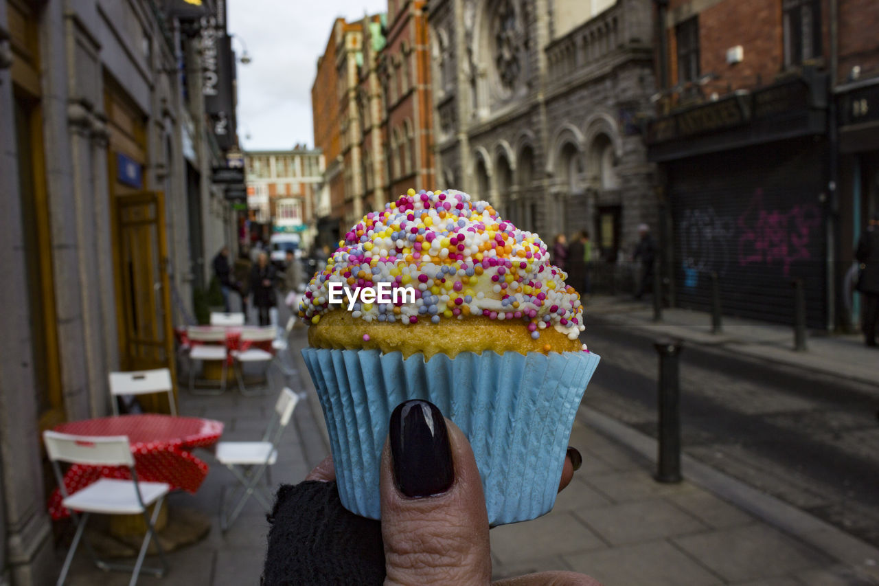 Close-up of hand holding cupcake against buildings