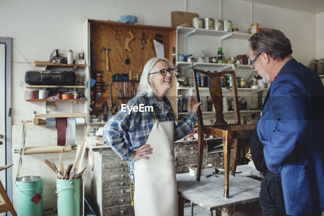 Smiling female owner showing wooden chair to customer at workshop