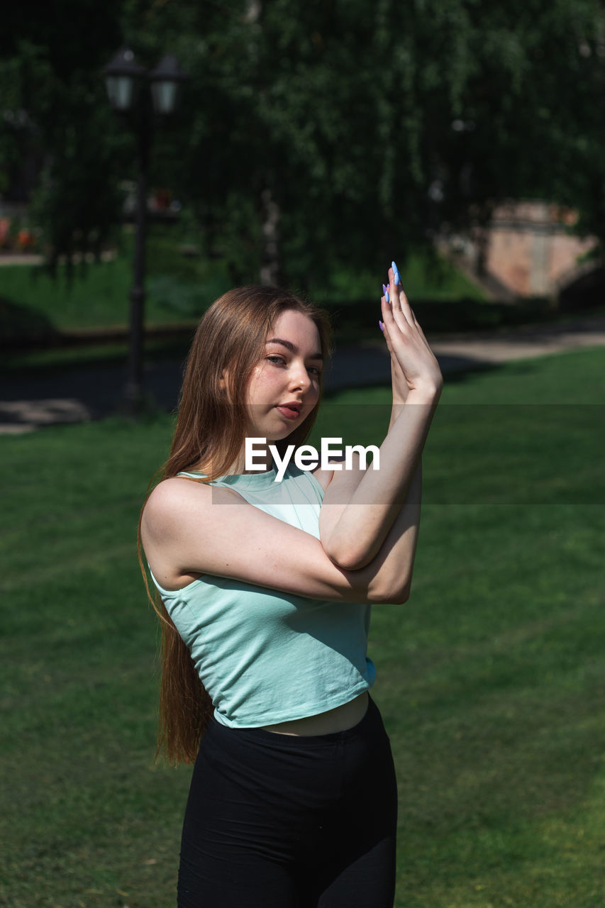 Young caucasian long-haired woman in sportswear is doing yoga in public park. outdoor workout. 