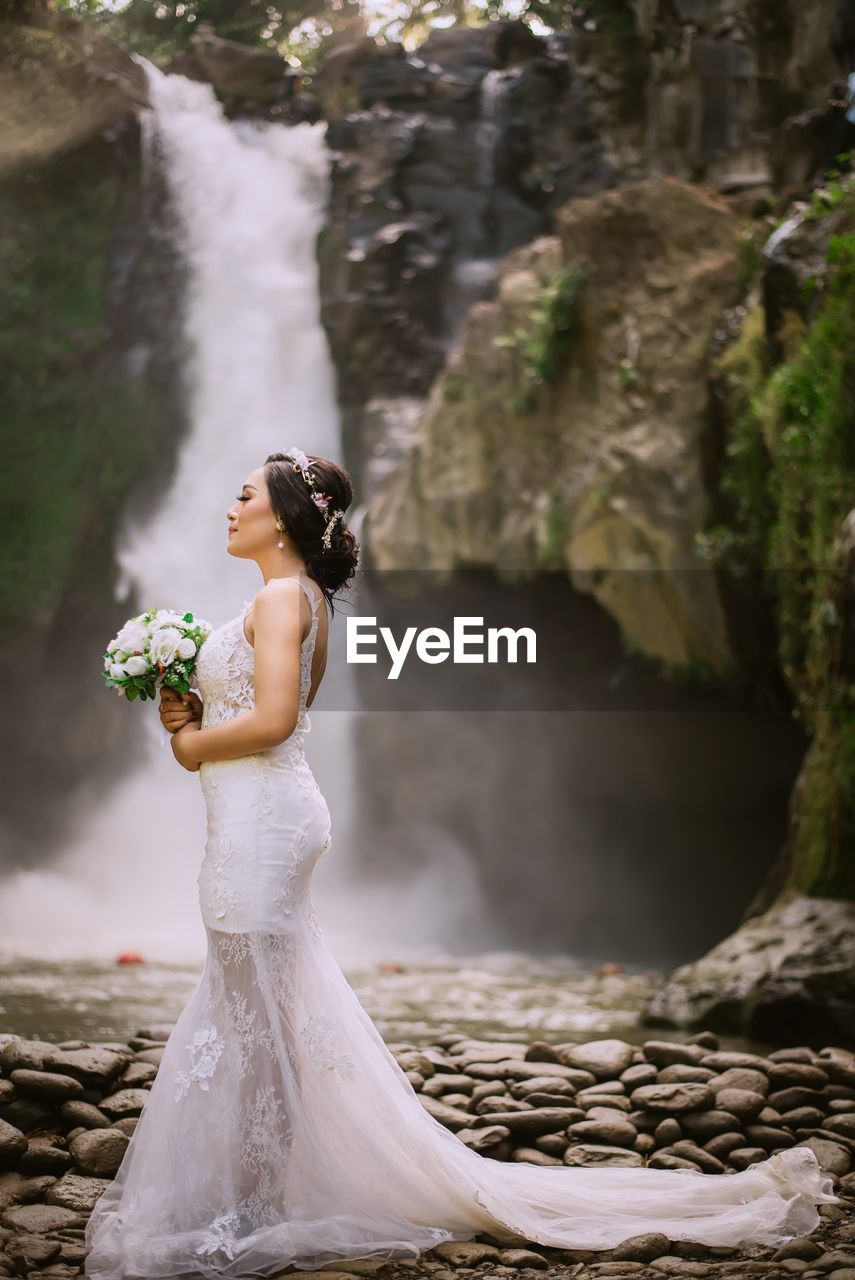 Close-up of woman standing on rock by waterfall