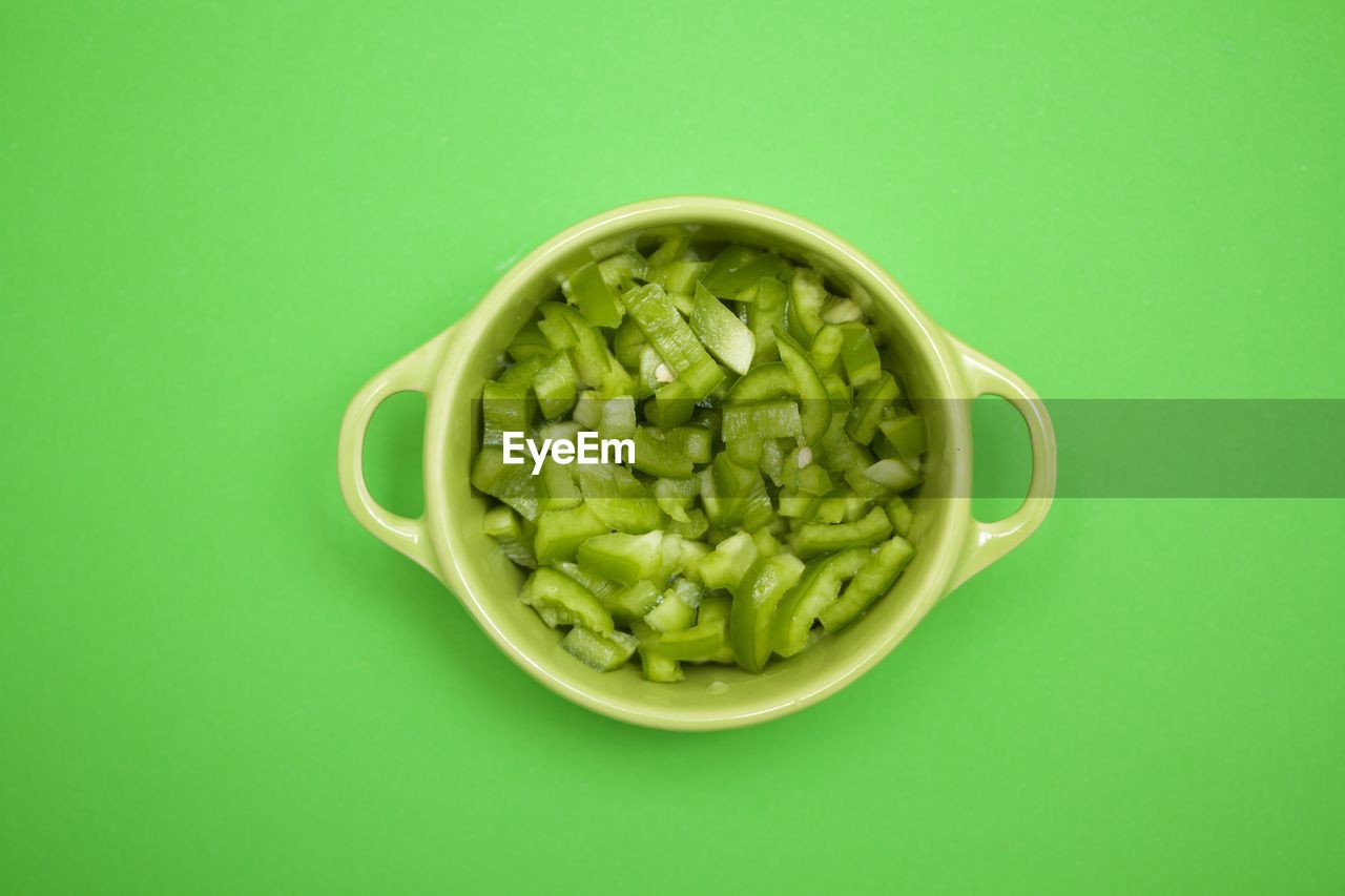Chopped green pepper in a green bowl on green background