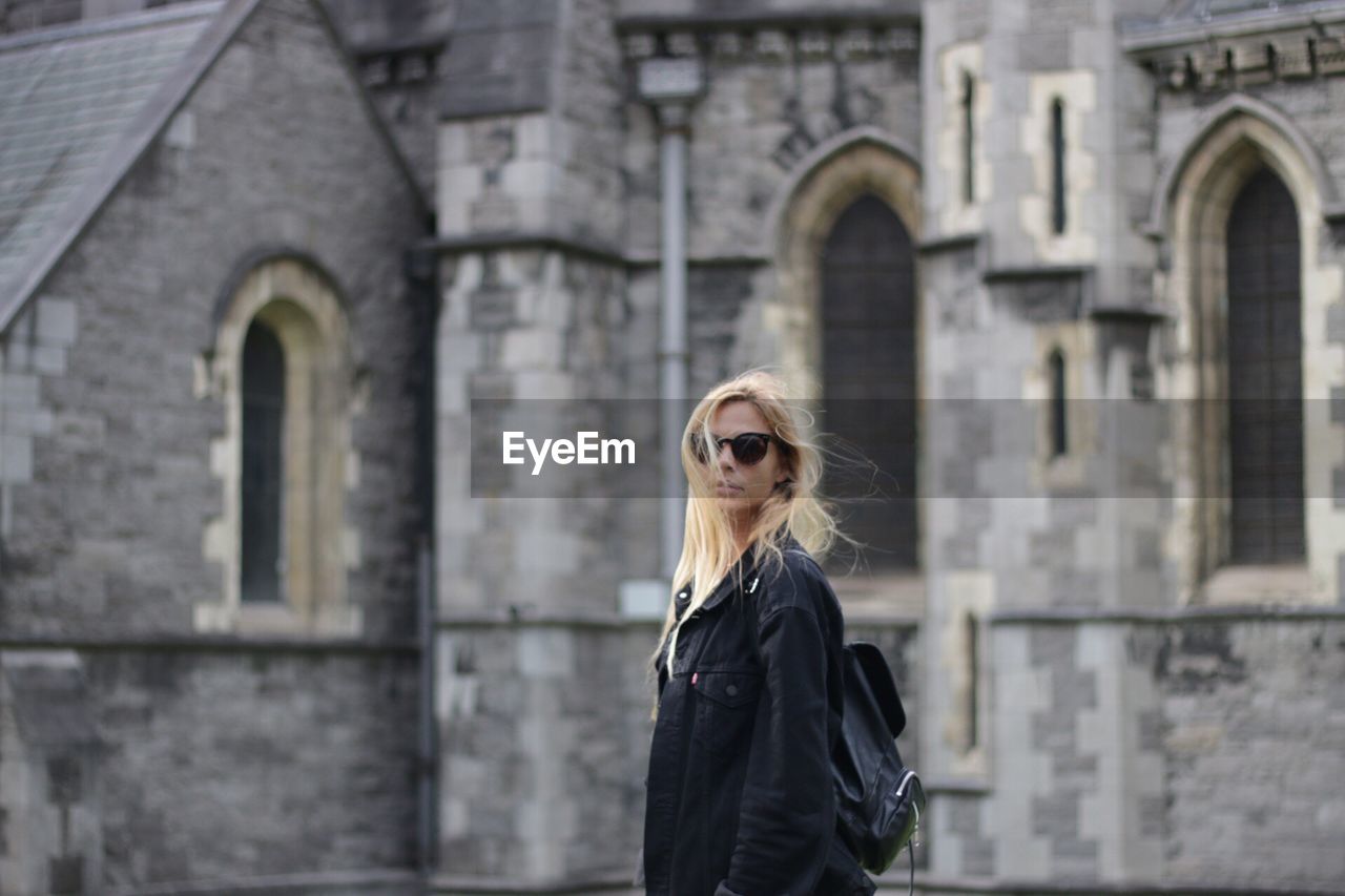 Portrait of young woman standing against building