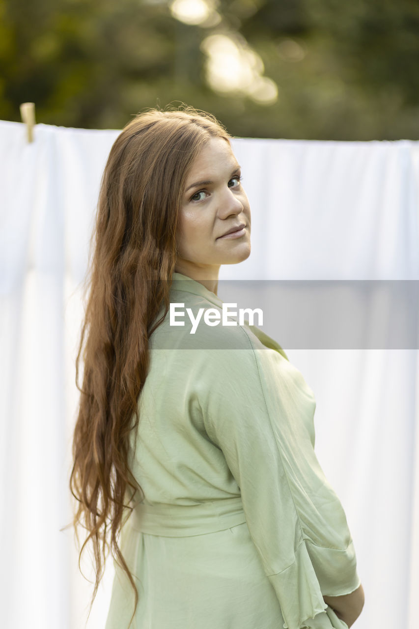 Caucasian pregnant woman hanging up laundry on clothes line outside, drying bed linens, bedding