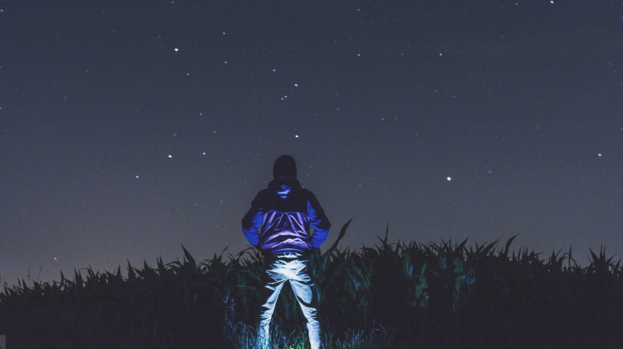 Rear view of hiker standing on field against star field