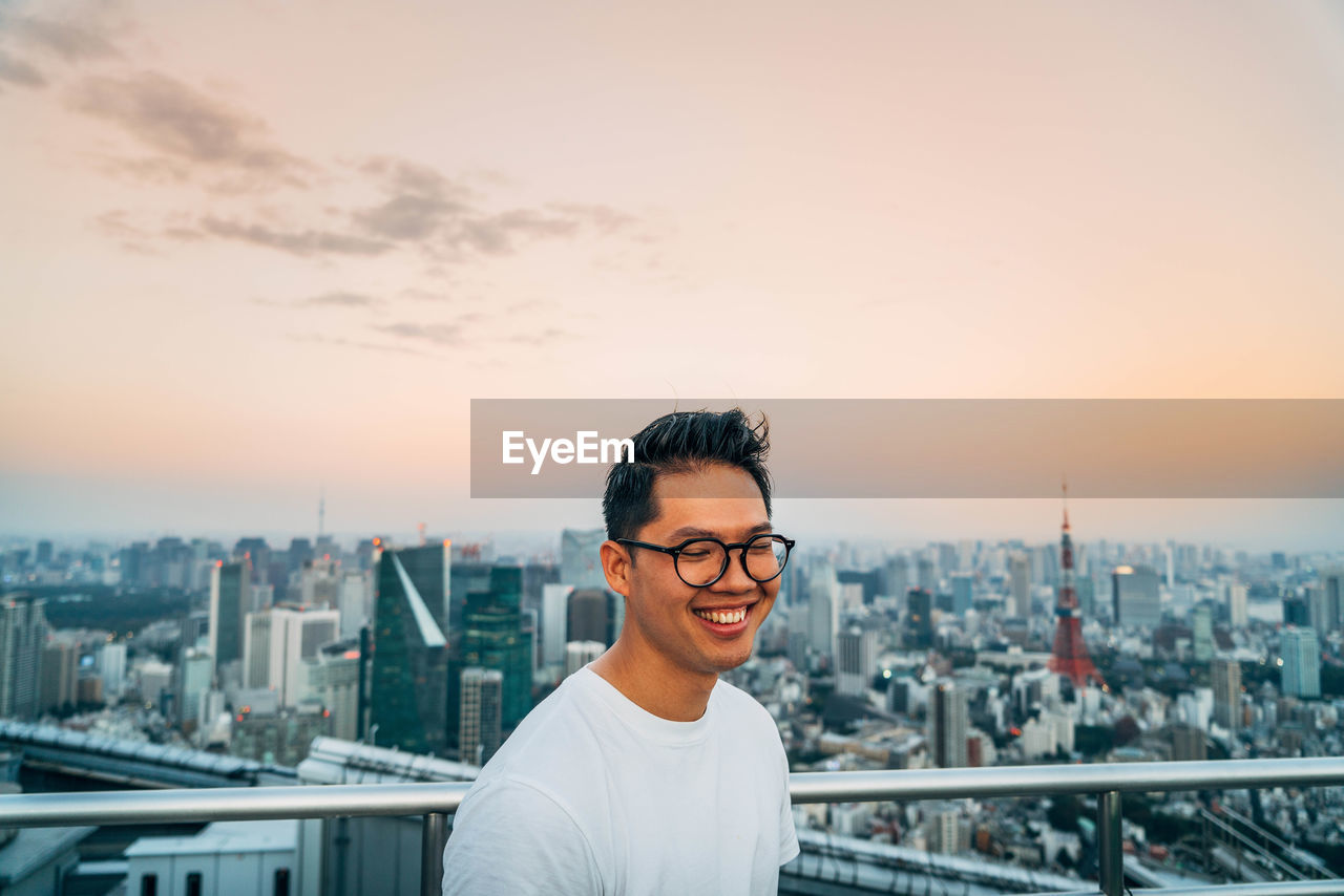 Smiling man standing at observation point against tokyo tower in city