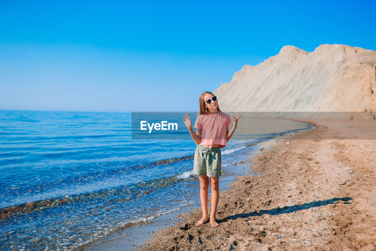 WOMAN STANDING ON BEACH AGAINST SKY