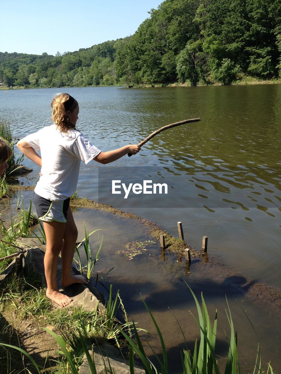 Full length of girl standing with stick at lakeshore