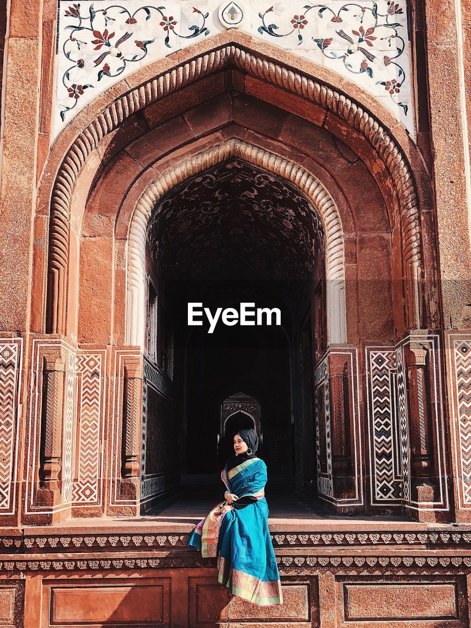 Woman wearing hijab sitting against historic building