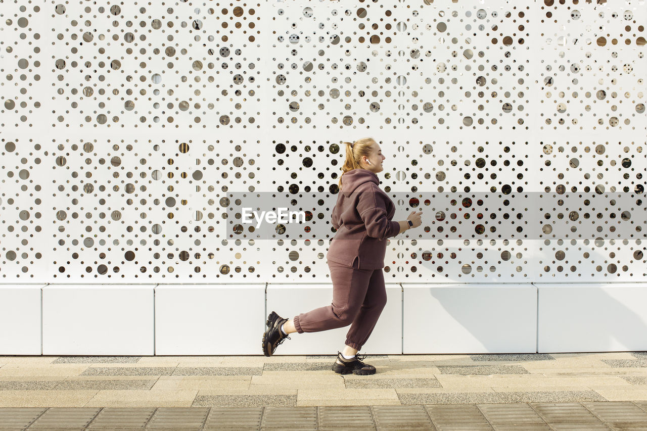 Overweight young woman jogging by wall