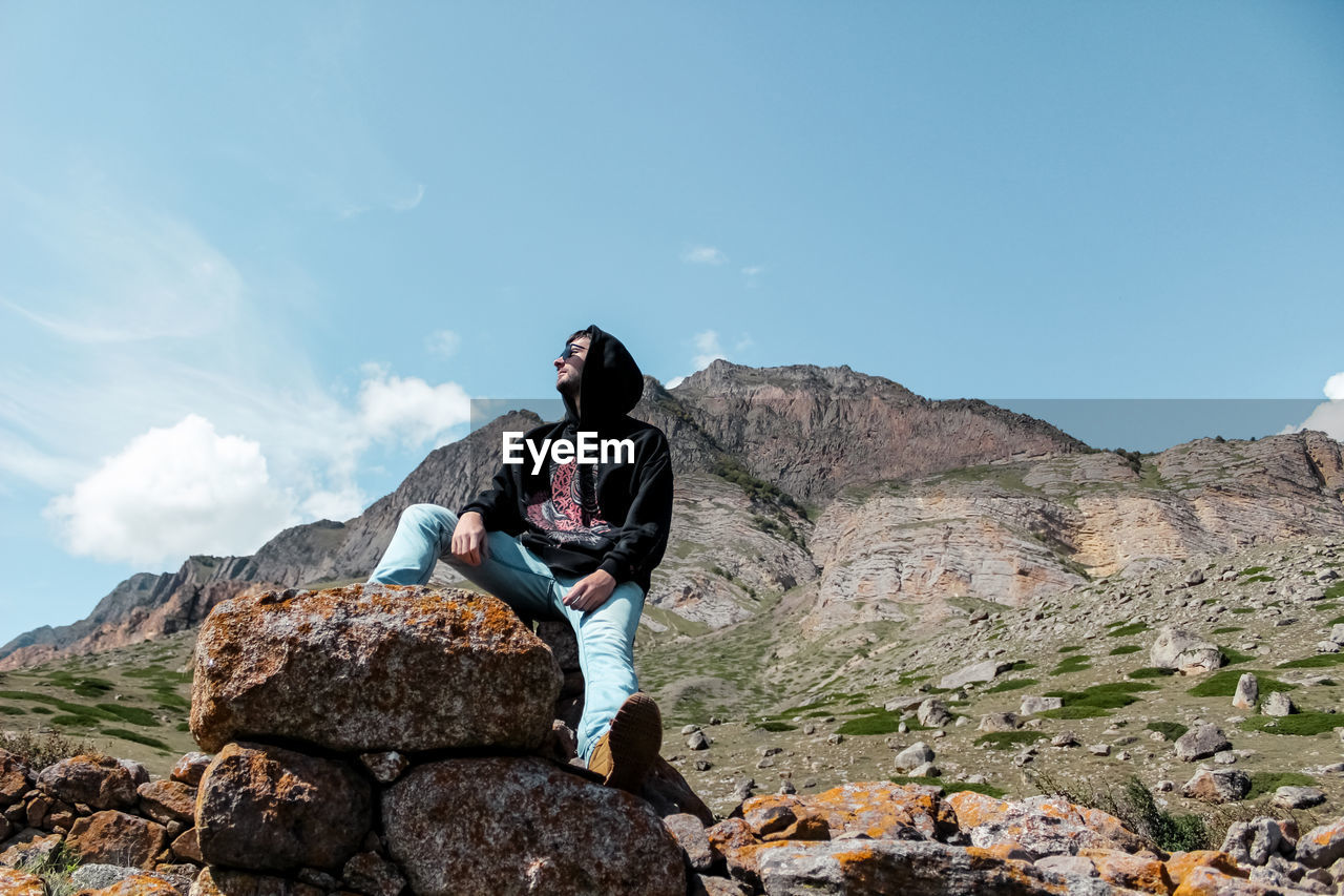 Low angle view of man sitting on rock against mountain