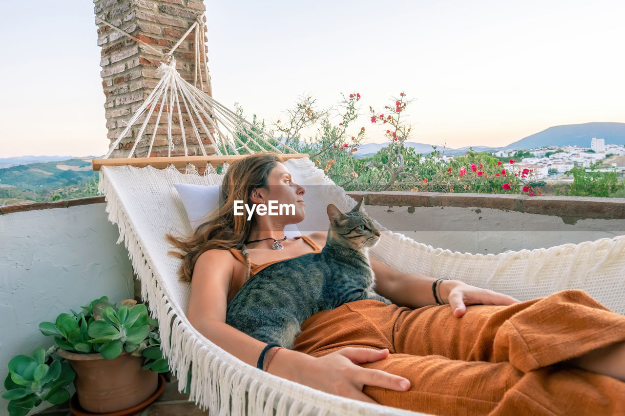 SIDE VIEW OF WOMAN SITTING ON HAMMOCK