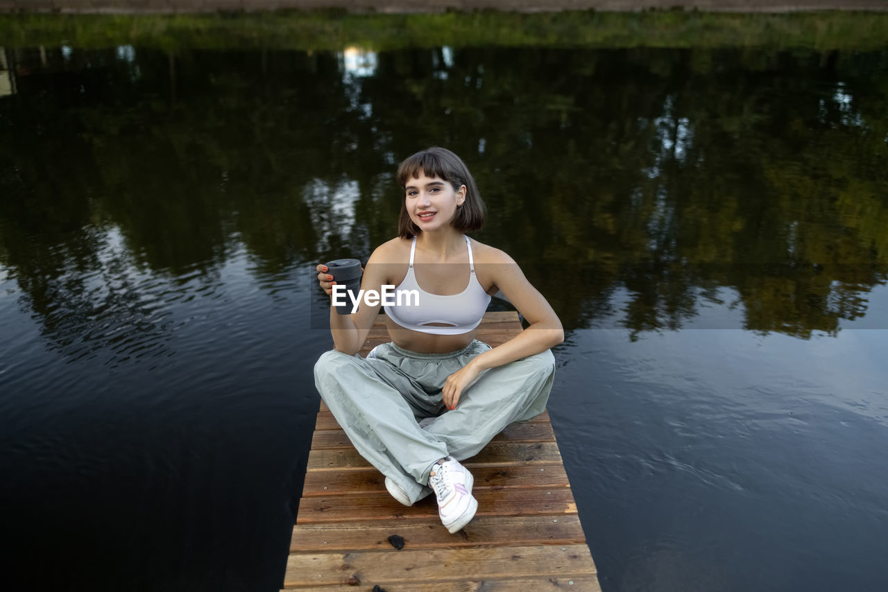 portrait of young woman sitting on pier over lake