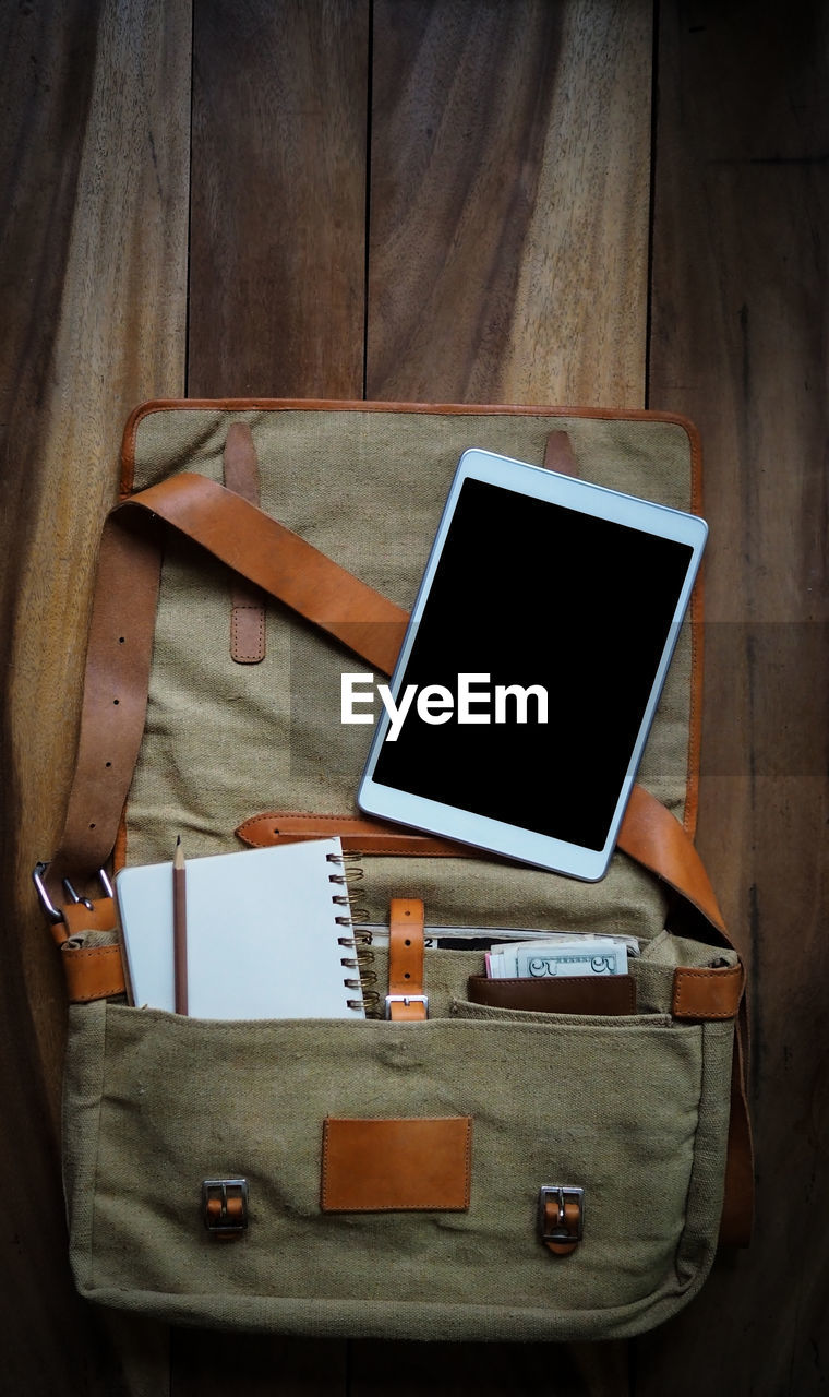 Directly above shot of digital tablet with book and pencil in bag on table