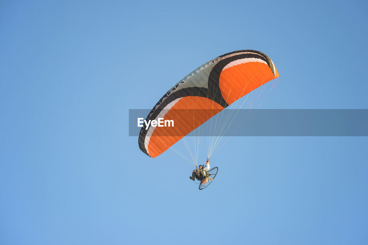 Low angle view of young man motor paragliding against clear sky