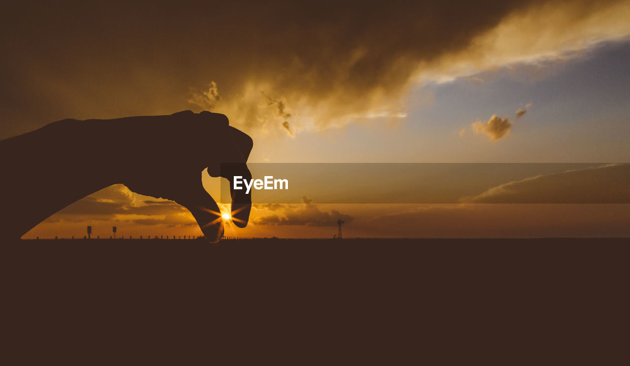 Optical illusion on person holding sun against cloudy sky during sunset