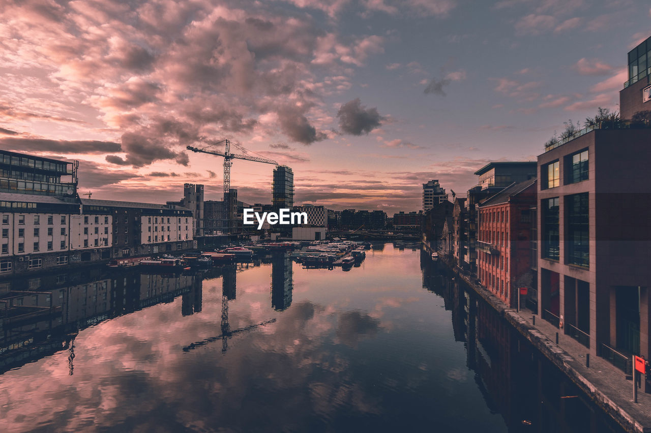 Canal amidst buildings against cloudy sky during sunset